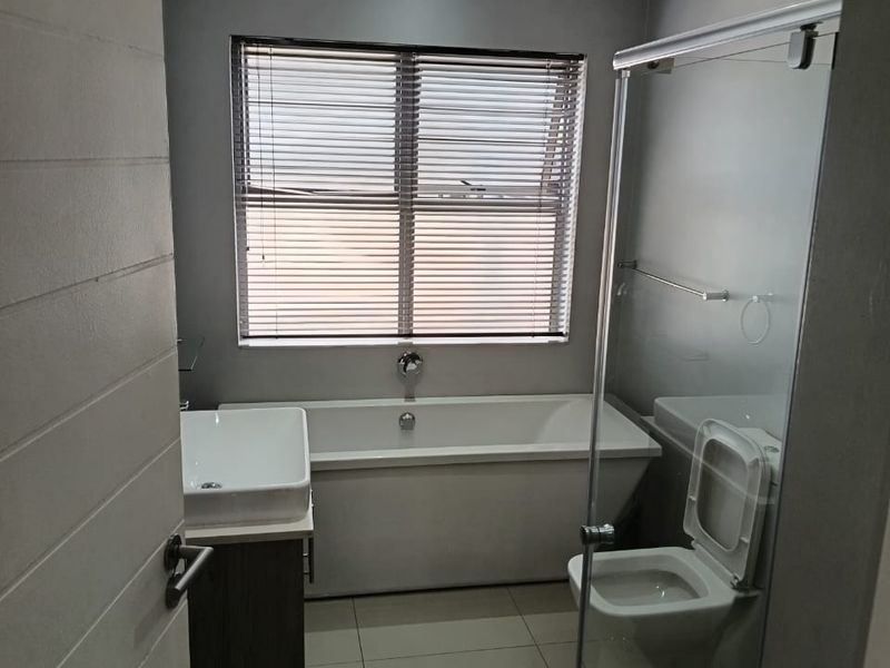 Modern bathroom featuring a freestanding bathtub, glass-enclosed shower, wall-mounted vanity with vessel sink, and neutral tiled finishes.