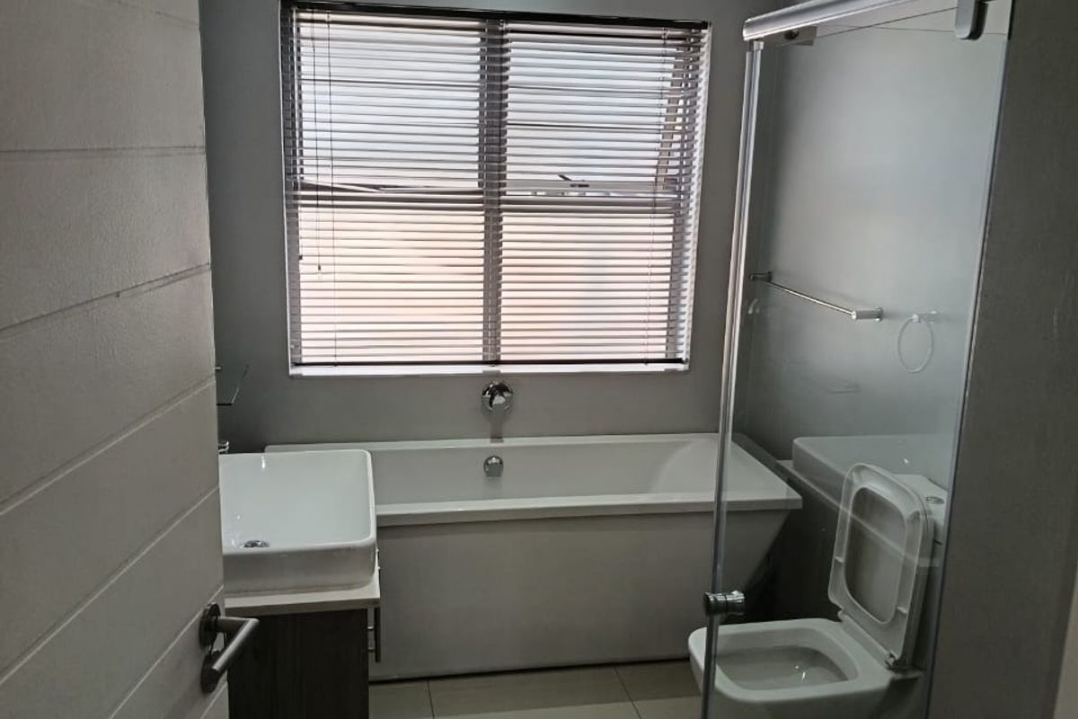 Modern bathroom featuring a freestanding bathtub, glass-enclosed shower, wall-mounted vanity with vessel sink, and neutral tiled finishes.