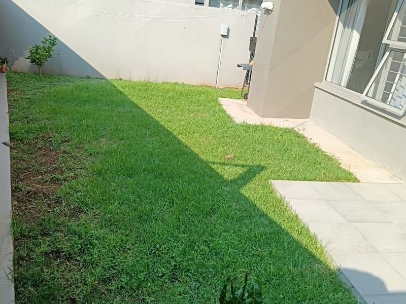 A private rear garden area featuring a small paved patio section and a grass lawn, enclosed by high boundary walls.