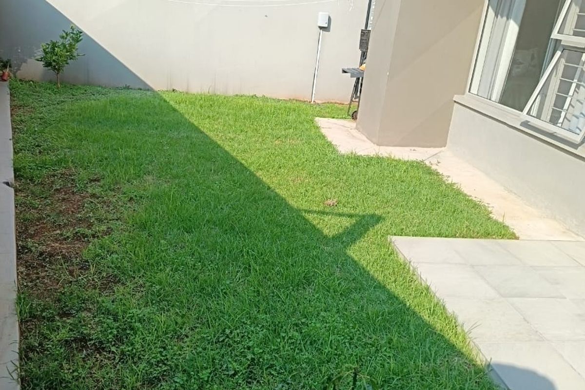 A private rear garden area featuring a small paved patio section and a grass lawn, enclosed by high boundary walls.