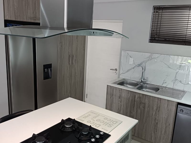 Modern kitchen featuring a central island with a gas hob, stainless steel extractor, stone countertops, marble-look splashback, and ample wood-grain cabinetry.