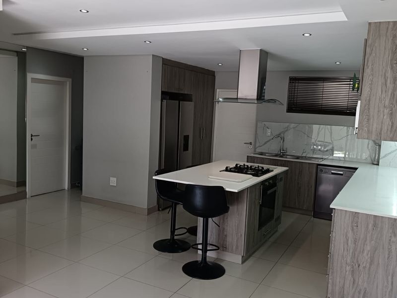 Modern kitchen featuring a central island with a gas hob, sleek cabinetry, marble-look backsplash, and high-quality tiled flooring with recessed lighting.
