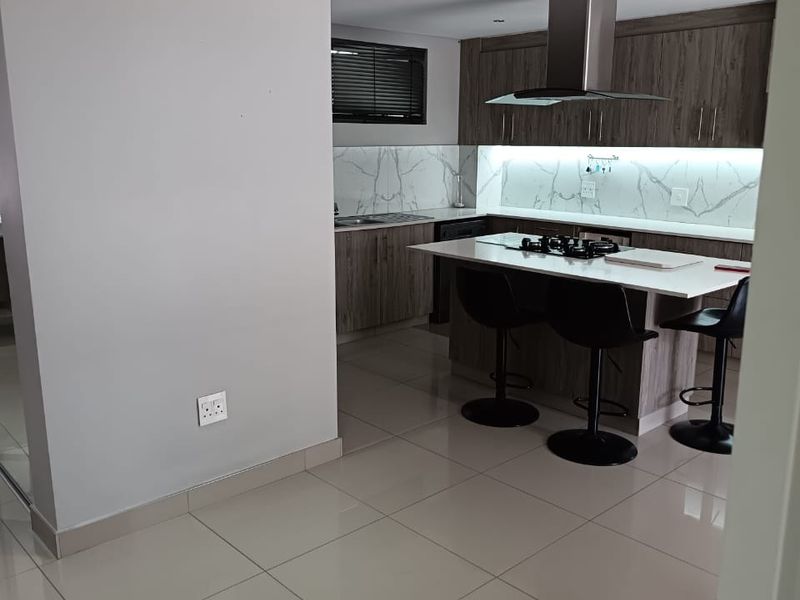 Modern kitchen featuring a central island with gas hob, extractor fan, sleek cabinetry, marble-look splashback, and recessed lighting.
