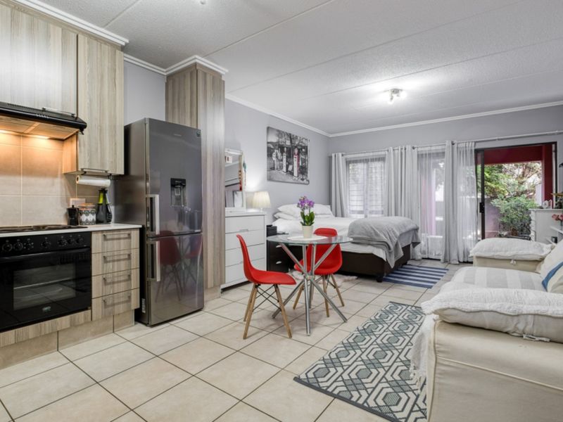 Open-plan studio apartment featuring a modern kitchen with built-in cabinetry, tiled flooring, and direct access to an outdoor patio area.