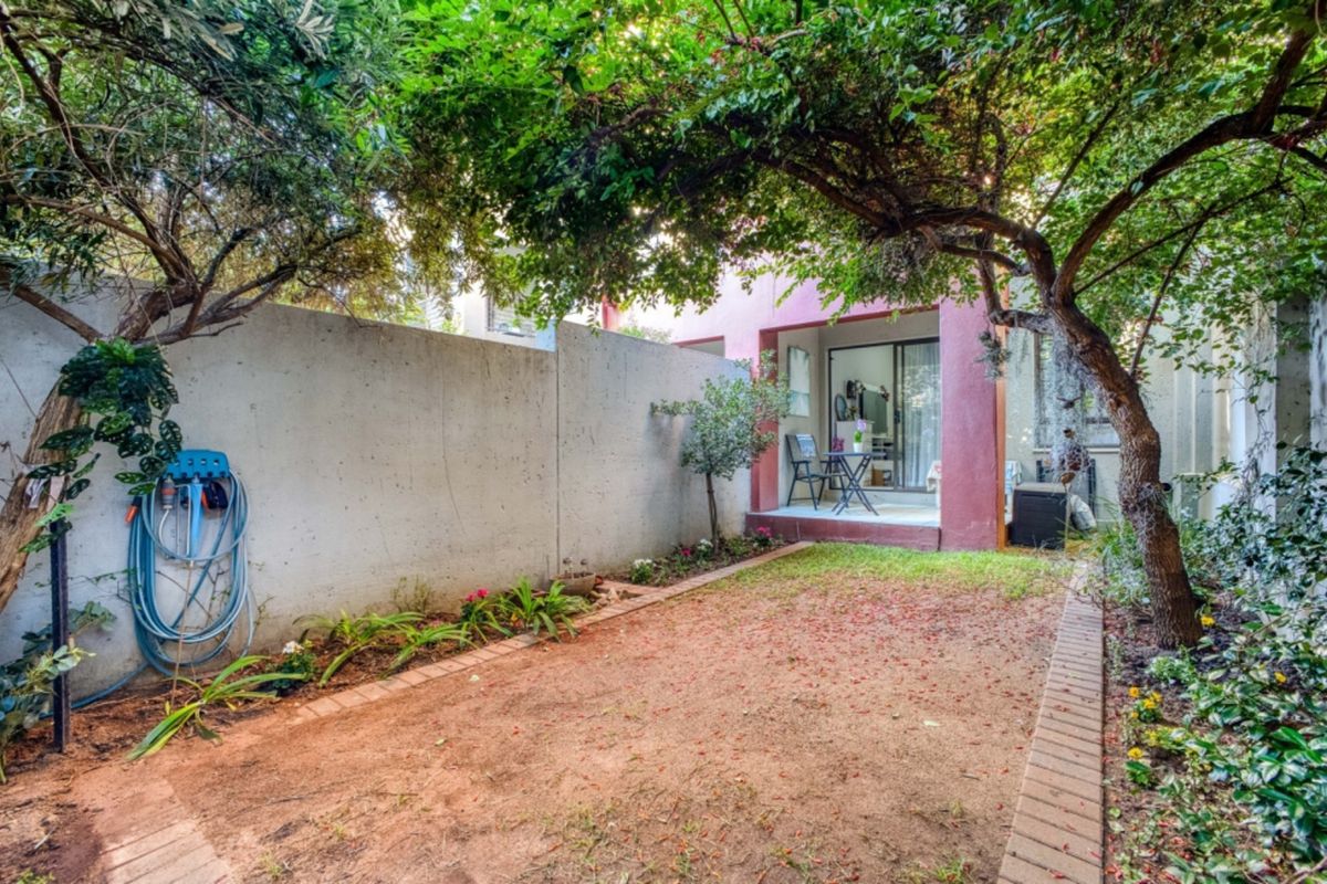 A private rear garden featuring a concrete boundary wall, brick-edged garden beds, and a covered patio area accessible via sliding glass doors.