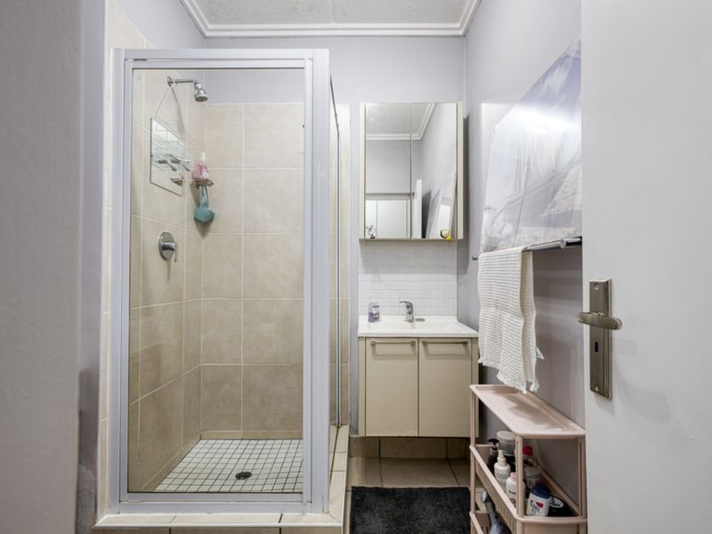 A functional bathroom featuring a glass-enclosed shower, a vanity unit with an integrated basin, and a mirrored medicine cabinet.