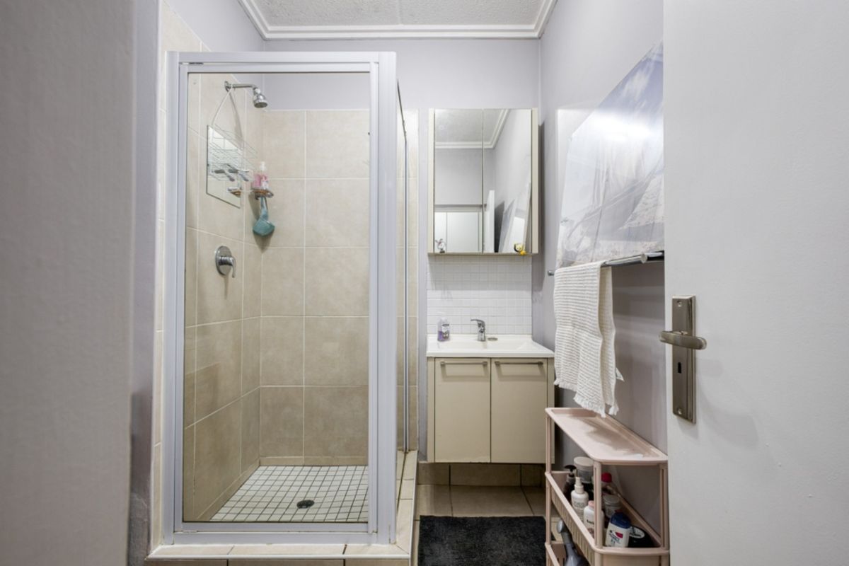 A functional bathroom featuring a glass-enclosed shower, a vanity unit with an integrated basin, and a mirrored medicine cabinet.