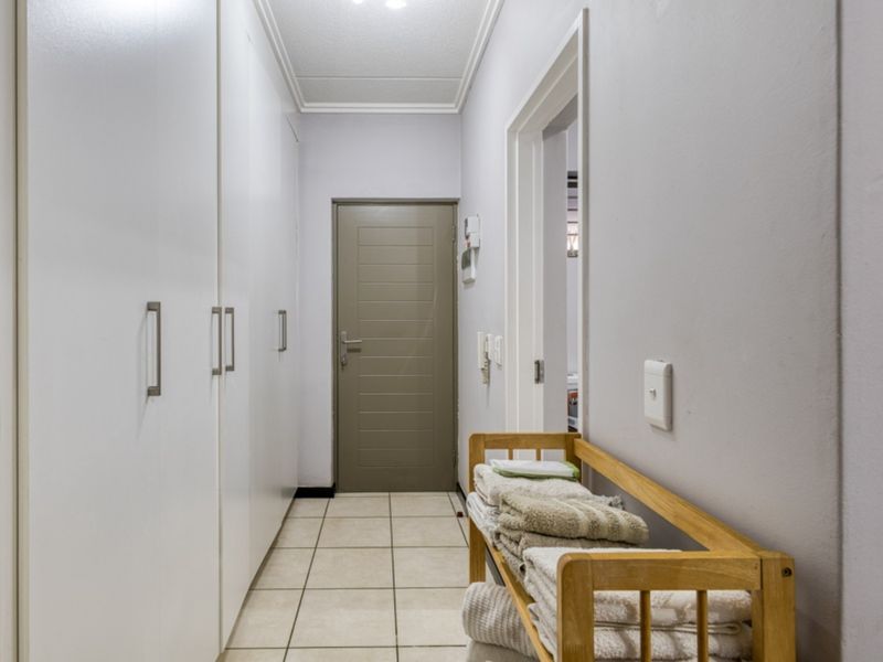A clean, well-lit hallway featuring neutral tiled flooring and extensive built-in storage cupboards along one wall.