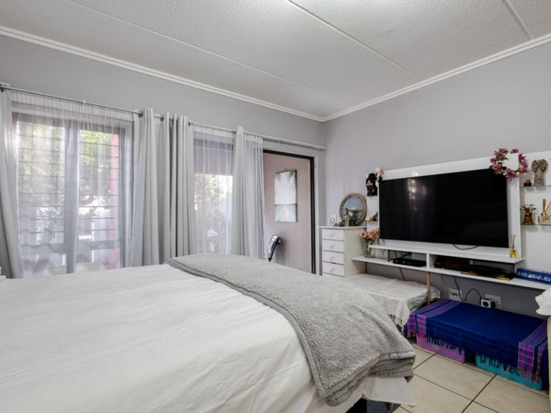 A bedroom featuring tiled flooring, a sliding glass door with security gate access to the exterior, and neutral wall finishes.