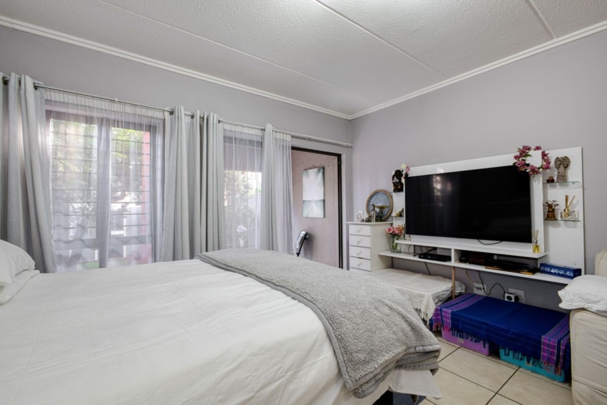 A bedroom featuring tiled flooring, a sliding glass door with security gate access to the exterior, and neutral wall finishes.