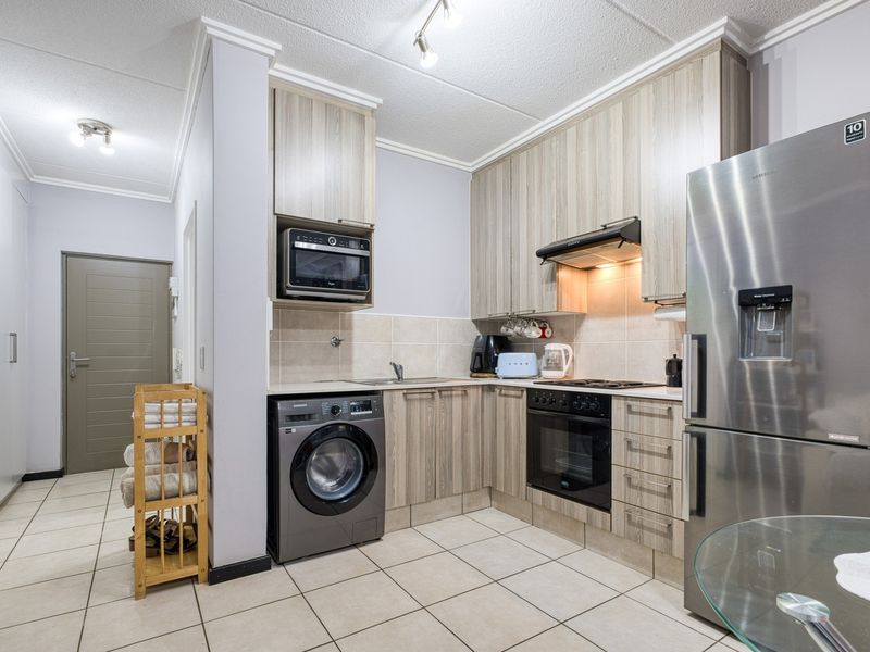 A functional kitchen featuring wood-look cabinetry, integrated appliances including an oven and microwave, tiled flooring, and a neutral tiled backsplash.