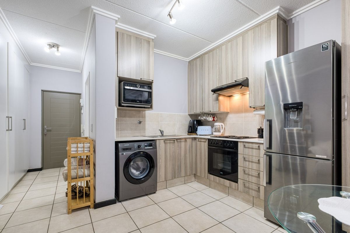 A functional kitchen featuring wood-look cabinetry, integrated appliances including an oven and microwave, tiled flooring, and a neutral tiled backsplash.