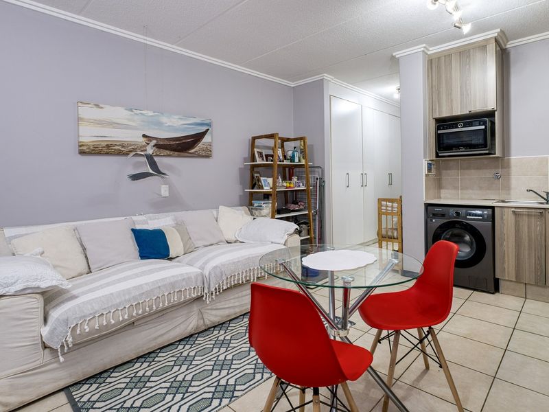 Open-plan living area featuring a compact kitchen with built-in cabinetry, microwave, and tiled flooring, seamlessly integrated with the living space.
