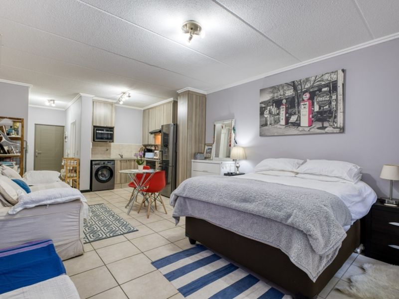 Open-plan studio apartment featuring a compact kitchen with built-in cabinetry and tiled flooring throughout the living and sleeping area.
