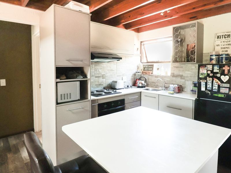 A functional kitchen featuring modern cabinetry, a stone-look backsplash, built-in appliances, and distinctive exposed timber ceiling beams.