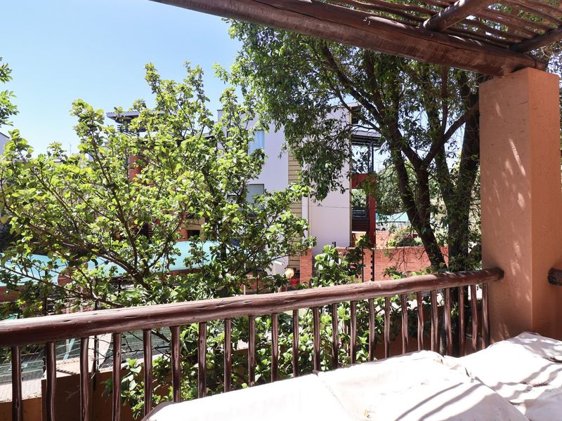 A covered balcony featuring a rustic timber pergola and railing, offering an elevated view of the surrounding complex and mature trees.