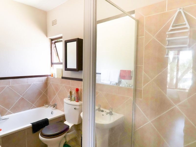 A functional bathroom featuring a bathtub, separate shower enclosure, pedestal basin, and toilet, finished with neutral wall tiling.
