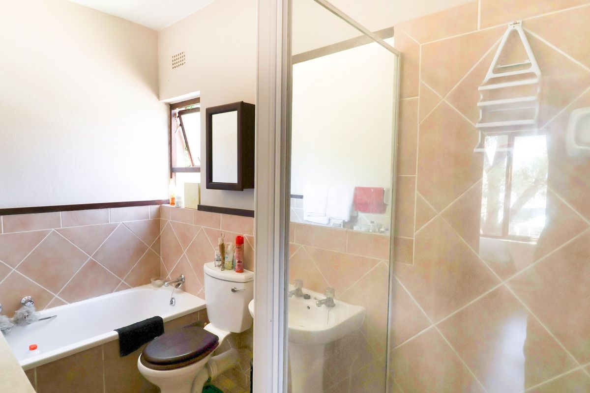 A functional bathroom featuring a bathtub, separate shower enclosure, pedestal basin, and toilet, finished with neutral wall tiling.