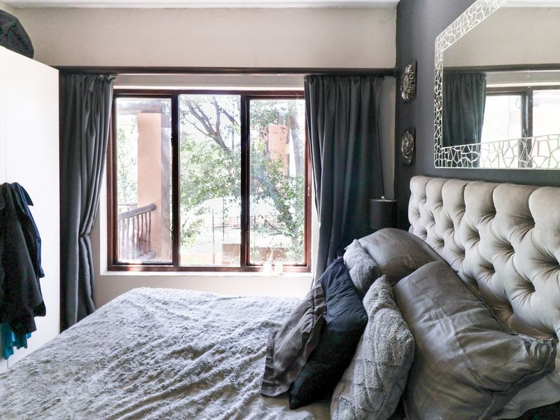 A cozy bedroom featuring a built-in wardrobe and a large window with views of the surrounding greenery.