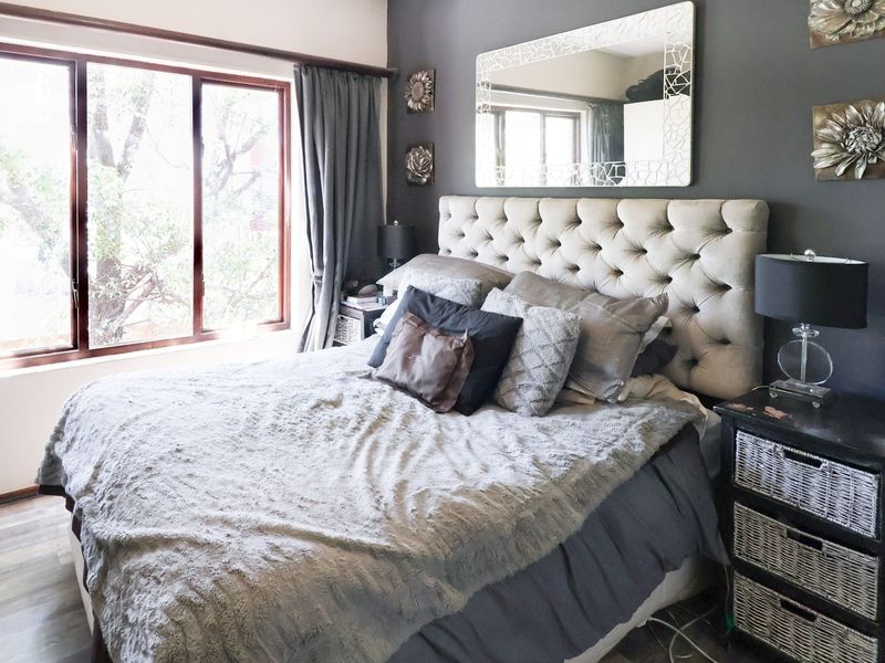 A well-lit bedroom featuring laminate flooring, a large window, and a dark grey accent wall.