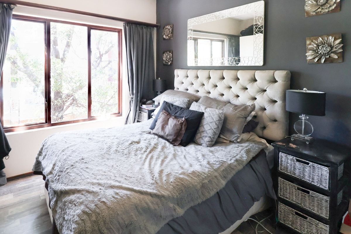 A well-lit bedroom featuring laminate flooring, a large window, and a dark grey accent wall.