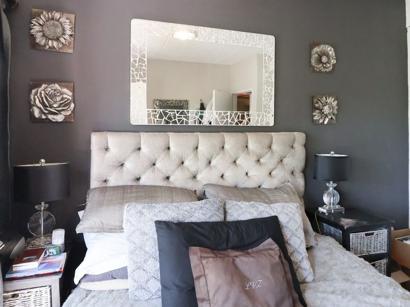 A bedroom featuring a dark accent wall, a tufted headboard, and a decorative wall mirror.