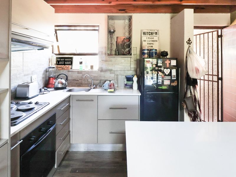 A functional kitchen featuring built-in cabinetry, a hob, oven, extractor fan, and a tiled backsplash, complemented by exposed timber ceiling beams.