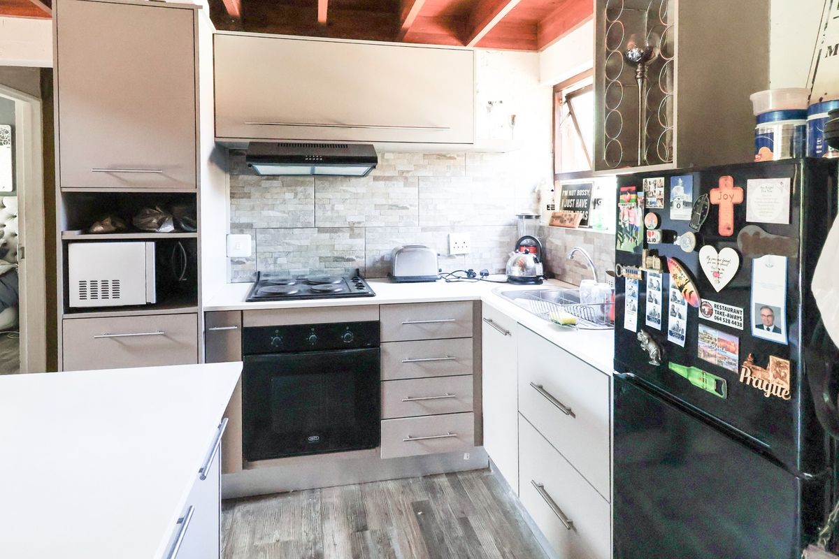 Compact kitchen featuring modern cabinetry, built-in oven and hob, stone tile backsplash, and exposed timber ceiling beams.
