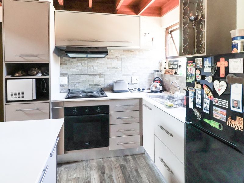Compact kitchen featuring modern cabinetry, built-in oven and hob, stone tile backsplash, and exposed timber ceiling beams.