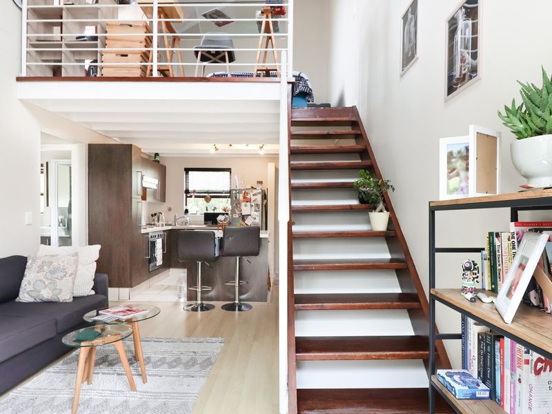 Open-plan living area featuring a modern kitchen, timber staircase leading to a mezzanine level, and light laminate flooring throughout.