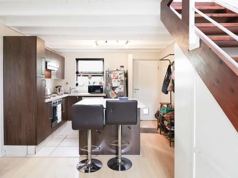 Open-plan kitchen and living area featuring dark wood cabinetry, a central island, and a wooden staircase leading to the upper level.