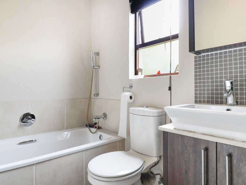 A well-maintained bathroom featuring a bathtub with shower mixer, a modern vessel sink on a vanity cabinet, and mosaic tile accents.