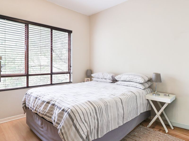 A well-lit bedroom featuring laminate flooring, neutral walls, and large windows fitted with venetian blinds.