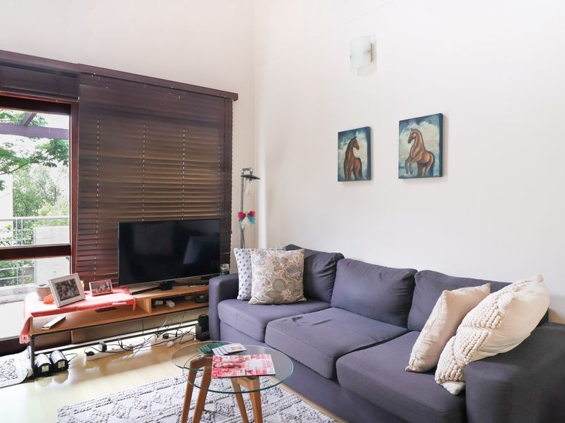 A bright living room featuring laminate flooring, neutral walls, and a large sliding glass door with timber venetian blinds leading to an outdoor area.