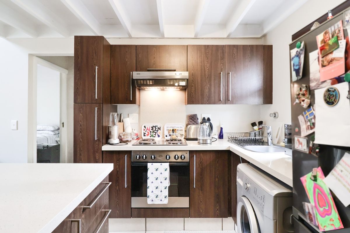 Compact kitchen featuring dark wood cabinetry, built-in oven and hob, stainless steel sink, and exposed white ceiling beams.