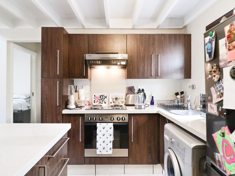 Compact kitchen featuring dark wood cabinetry, built-in oven and hob, stainless steel sink, and exposed white ceiling beams.