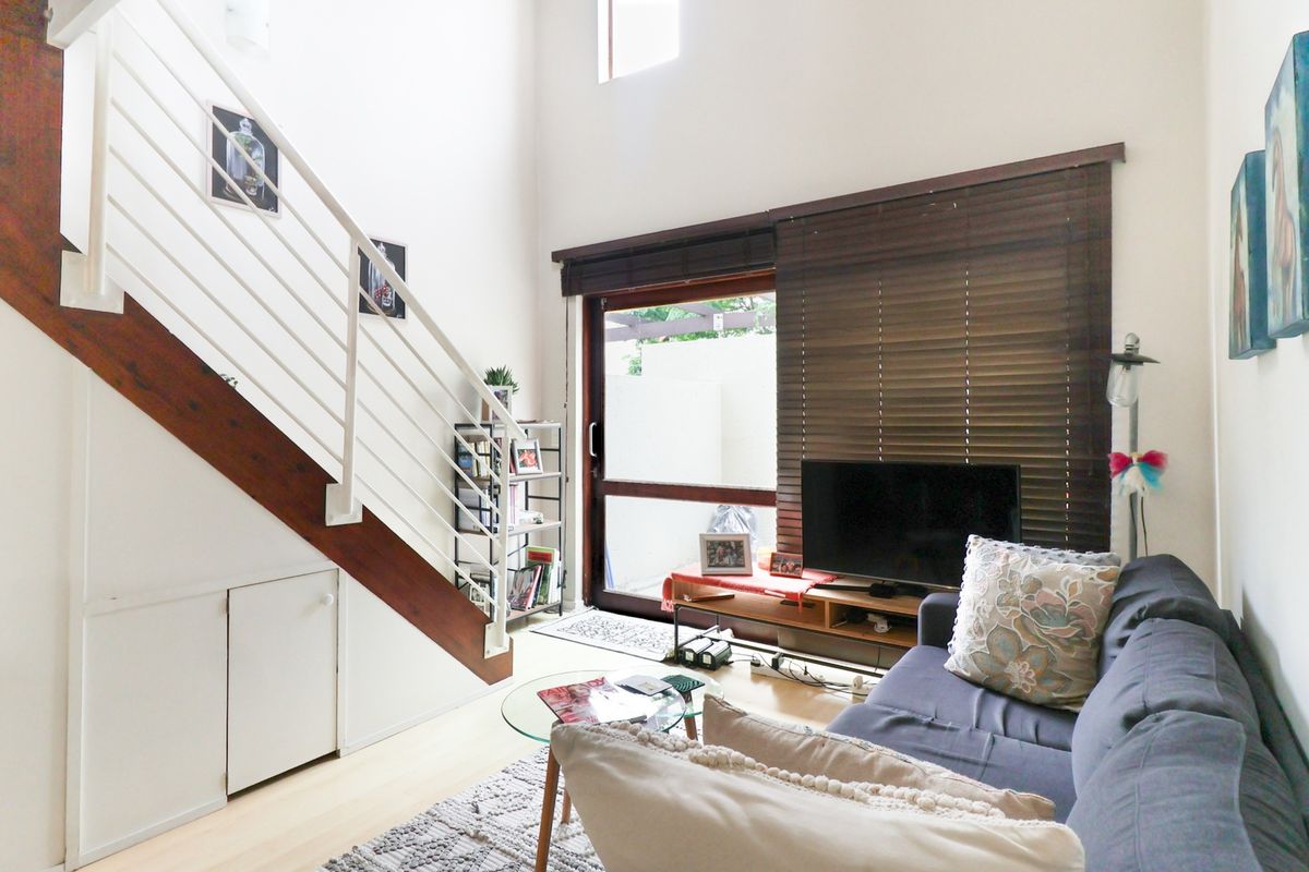 A bright living room featuring a staircase with under-stair storage, laminate flooring, and a sliding glass door leading to an outdoor area.