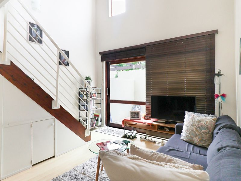 A bright living room featuring a staircase with under-stair storage, laminate flooring, and a sliding glass door leading to an outdoor area.