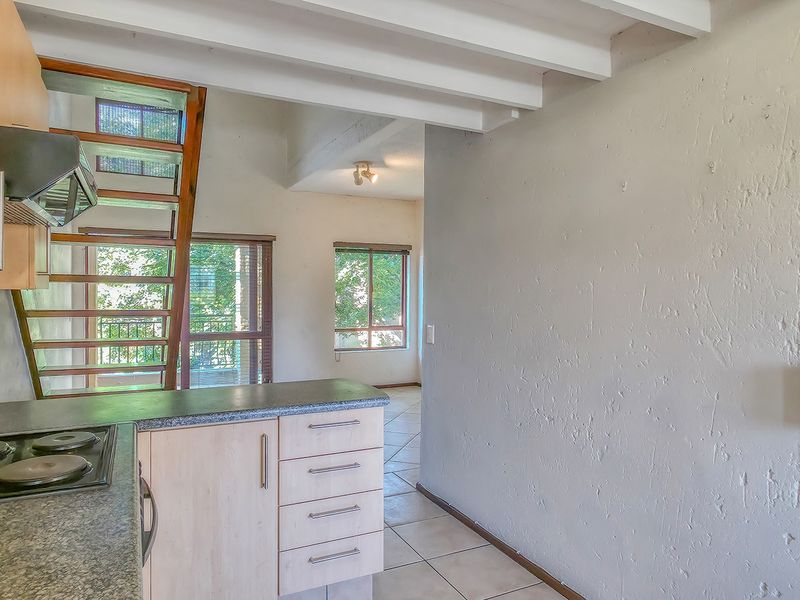 Open plan kitchen area featuring light wood cabinetry, electric hob, tiled flooring, and an exposed wooden staircase leading to the upper level.