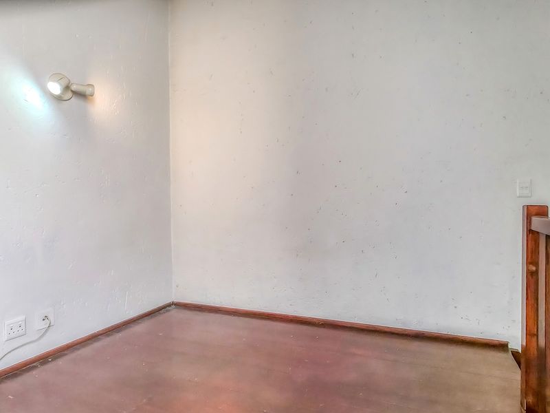 An empty landing or hallway area featuring a wooden balustrade, wall-mounted lighting, and worn flooring, offering a blank canvas for interior updates.
