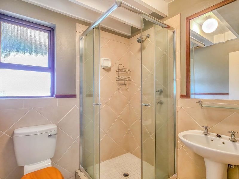 A functional bathroom featuring a glass-enclosed shower, pedestal sink, and toilet, finished with neutral wall tiles and a large vanity mirror.