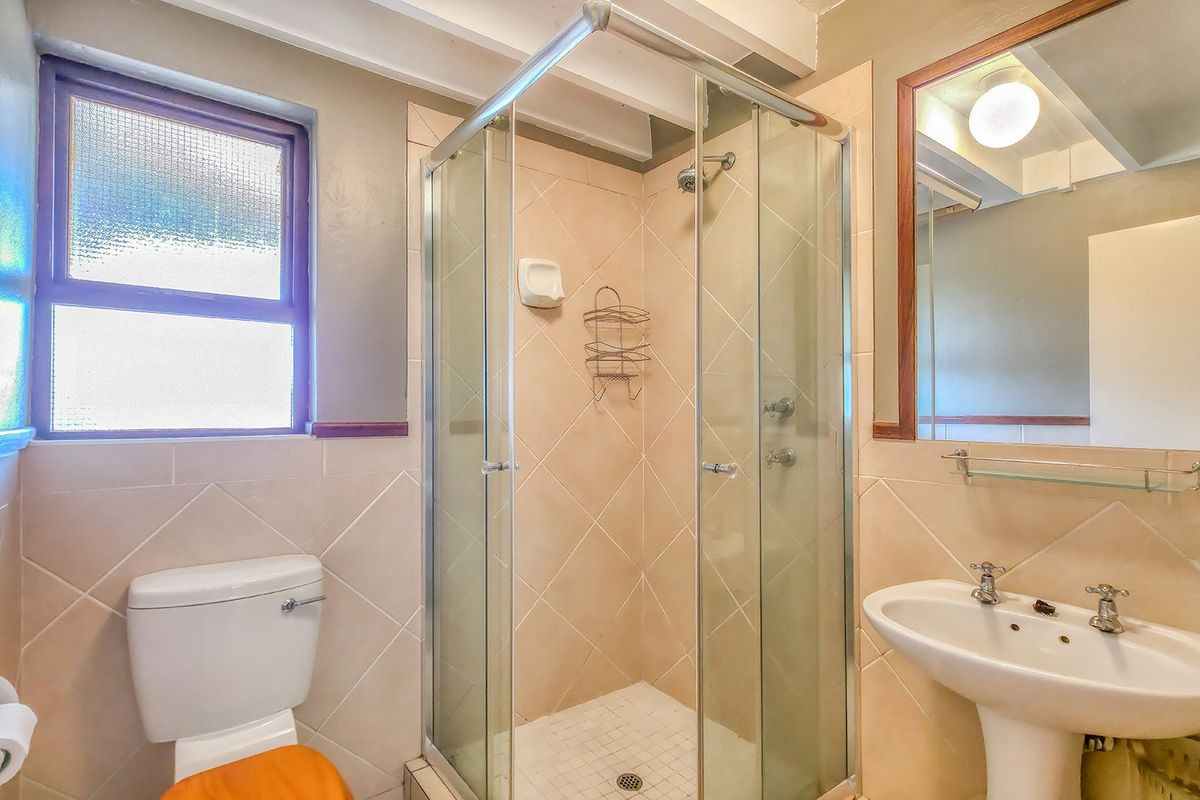 A functional bathroom featuring a glass-enclosed shower, pedestal sink, and toilet, finished with neutral wall tiles and a large vanity mirror.