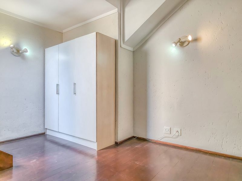A bedroom featuring wooden flooring, a built-in wardrobe, and wall-mounted lighting fixtures, offering a functional space with potential for cosmetic updates.