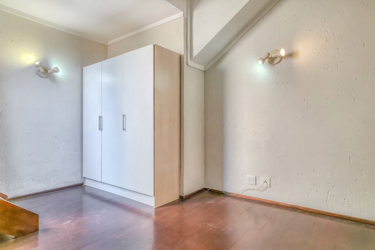 A bedroom featuring wooden flooring, a built-in wardrobe, and wall-mounted lighting fixtures, offering a functional space with potential for cosmetic updates.