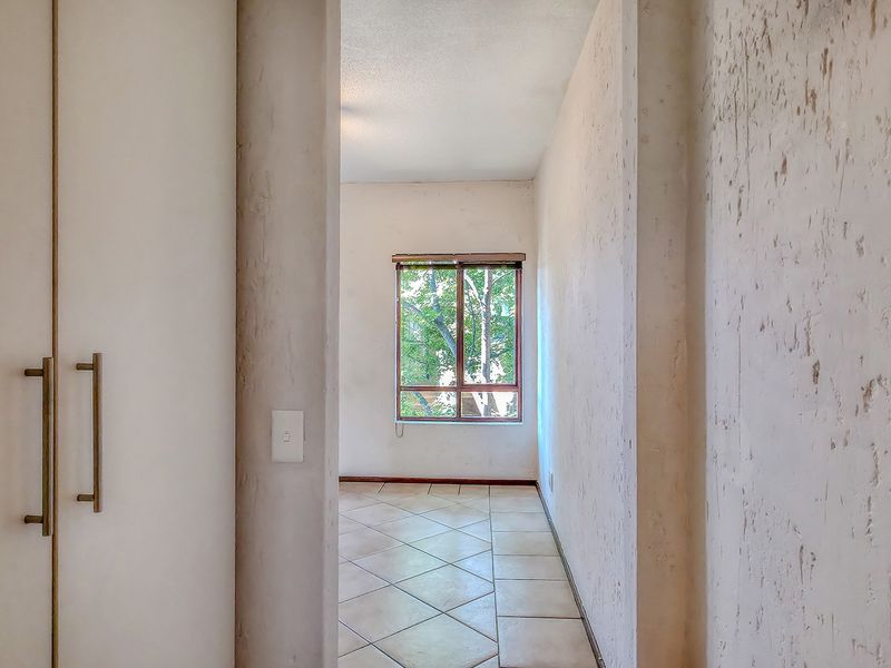A vacant hallway featuring built-in cupboards, tiled flooring, and a window providing natural light.