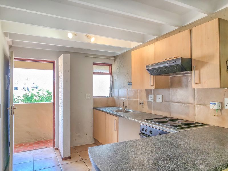 Functional kitchen featuring built-in cabinetry, electric hob, extractor fan, and tiled backsplash, with direct access to an outdoor balcony area.