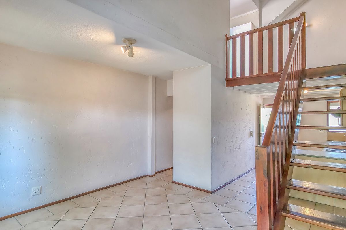 An empty living area featuring tiled flooring and a wooden staircase with a balustrade, leading to an upper level.