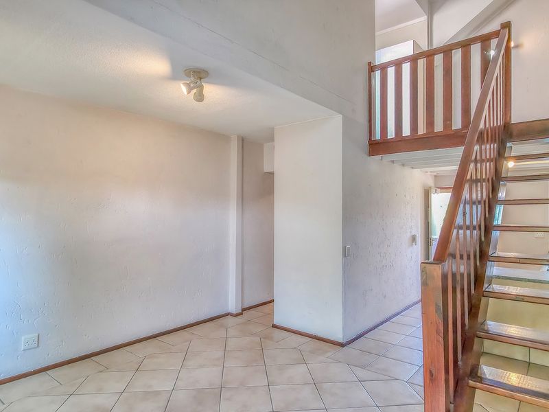 An empty living area featuring tiled flooring and a wooden staircase with a balustrade, leading to an upper level.