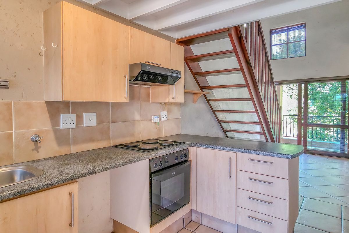 Compact kitchen featuring light wood cabinetry, granite countertops, built-in oven and hob, with an adjacent wooden staircase leading to the upper level.