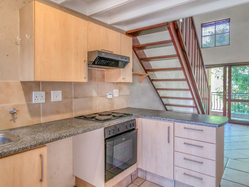 Compact kitchen featuring light wood cabinetry, granite countertops, built-in oven and hob, with an adjacent wooden staircase leading to the upper level.